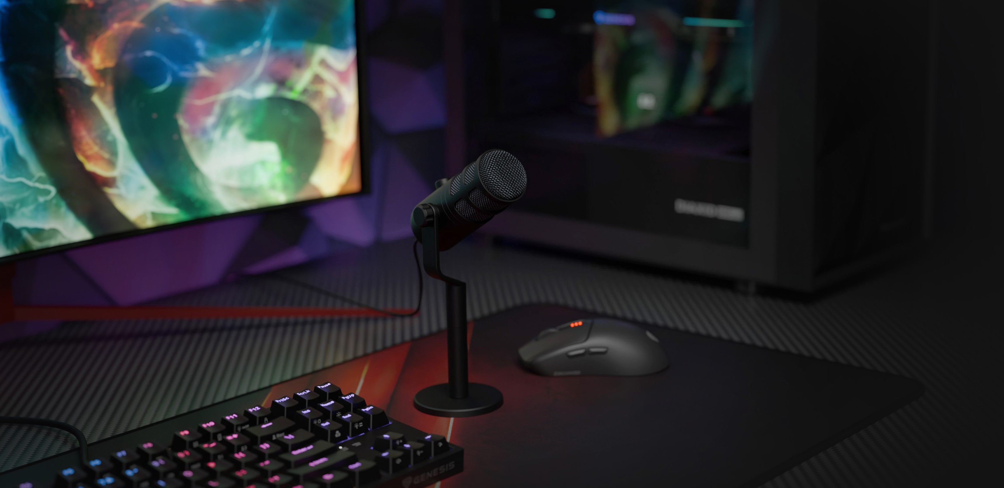 Dynamický mikrofon USB na stojanu s klávesnicí a myší na pozadí barevného herního monitoru.